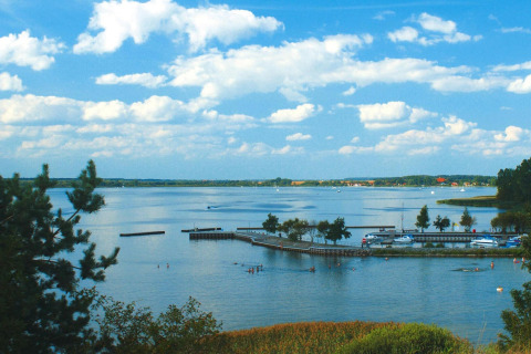 Uitzicht vanaf de woonboot 'Watercamper deluxe' in Duitsland met bomen, meer en blauwe lucht.