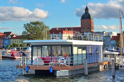 Moderne Hausboot 'Blue Active' im Hafen von Ribnitz-Damgarten mit Stadt und Kirchturm im Hintergrund.