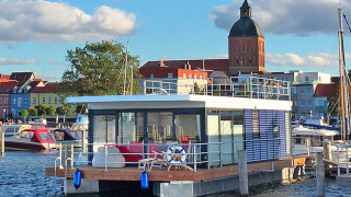 Casa flotante moderna 'Blue Active' en el puerto de Ribnitz-Damgarten con vista a la ciudad y la iglesia.