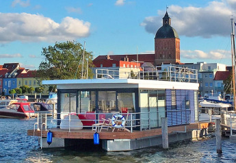 Casa flotante moderna 'Blue Active' en el puerto de Ribnitz-Damgarten con vista a la ciudad y la iglesia.
