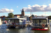 Maisons flottantes à Ribnitz-Damgarten, Allemagne, avec la ville et un clocher d’église en arrière-plan.