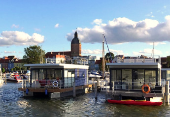 Casa flotante en el puerto de Ribnitz-Damgarten, Alemania, con la ciudad y torre de iglesia al fondo.