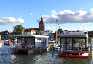 Casa flotante en el puerto de Ribnitz-Damgarten, Alemania, con la ciudad y torre de iglesia al fondo.