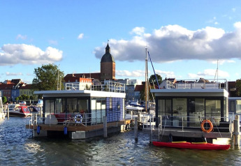 Casa flotante en el puerto de Ribnitz-Damgarten, Alemania, con la ciudad y torre de iglesia al fondo.