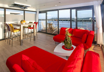 Salon moderne sur une péniche avec canapés rouges, table à manger et vue sur l'eau à Ribnitz-Damgarten, Allemagne.