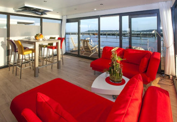 Modernes Wohnzimmer auf einem Hausboot mit roten Sofas, Esstisch und Wasserblick in Ribnitz-Damgarten, Deutschland.