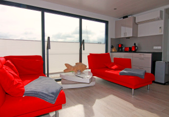 Modernes Hausboot-Wohnzimmer mit roten Sofas, Küchenbereich und großen Fenstern in Ribnitz-Damgarten.