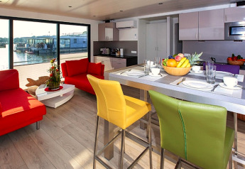 Salón moderno y cocina en una casa flotante con sillas y sofás coloridos, vista al agua en Alemania.