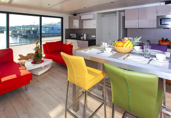 Salón moderno y cocina en una casa flotante con sillas y sofás coloridos, vista al agua en Alemania.