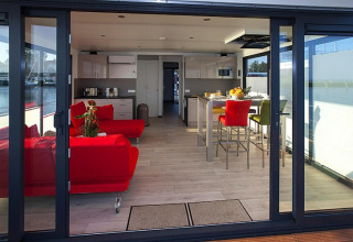 Salon et cuisine modernes sur une péniche avec canapés rouges et coin repas, vus de la terrasse.