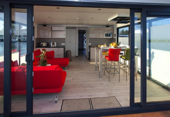 Sala y cocina modernas en una casa flotante con sofás rojos y comedor, vista desde la terraza.