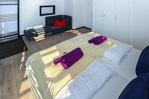 Modernes Schlafzimmer auf einem Hausboot mit Doppelbett, lila Handtüchern und Sofa in Deutschland.