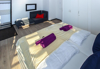 Dormitorio moderno en una casa flotante con cama doble, toallas moradas, sofá y armarios blancos.
