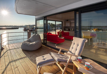 Pont ensoleillé de la péniche Floating Houses Blue Active avec fauteuils lounge et vue sur l’eau.