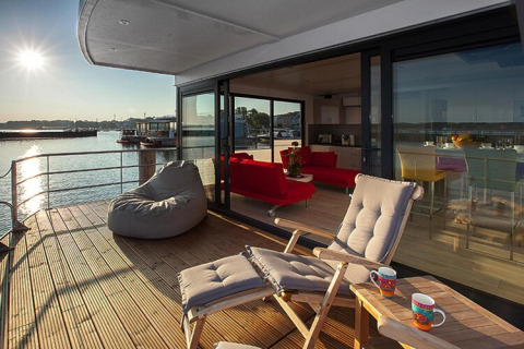 Sonnige Terrasse auf Hausboot Floating Houses Blue Active mit Lounge, Seeblick und gemütlicher Sitzecke.