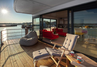 Pont ensoleillé de la péniche Floating Houses Blue Active avec fauteuils lounge et vue sur l’eau.