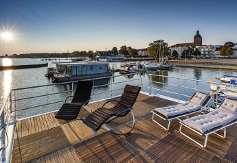 Sunny deck view from the Floating Houses Blue Active houseboat in Ribnitz-Damgarten, Germany, with lounge chairs.