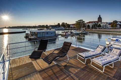 Vista soleada desde la cubierta del houseboat Floating Houses Blue Active en Ribnitz-Damgarten, Alemania, con tumbonas.