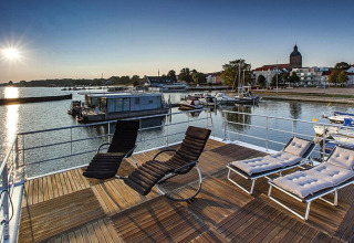 Vue ensoleillée de la terrasse du houseboat Floating Houses Blue Active à Ribnitz-Damgarten, Allemagne, avec transats.