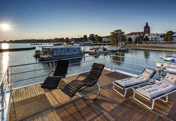 Sonnige Terrasse auf dem Hausboot Floating Houses Blue Active in Ribnitz-Damgarten mit Blick auf den Hafen.