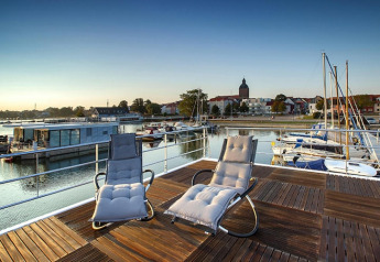 Zwei Liegestühle auf dem Deck eines Hausboots mit Blick auf den Hafen in Ribnitz-Damgarten, Deutschland.