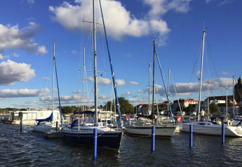 Veleros y casas flotantes atracados en el puerto de Ribnitz-Damgarten, Alemania, bajo el cielo azul.
