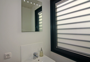 Modern bathroom with mirror, sink, soap dispenser and large window with blinds on a houseboat.