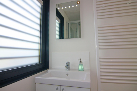 Salle de bain moderne avec miroir, lavabo, distributeur de savon et grande fenêtre sur la péniche Floating Houses Blue Active, Allemagne.