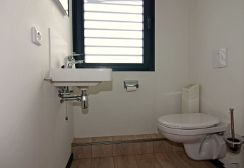 Baño moderno en una casa flotante de Alemania con inodoro mural, lavabo compacto y ventana grande.