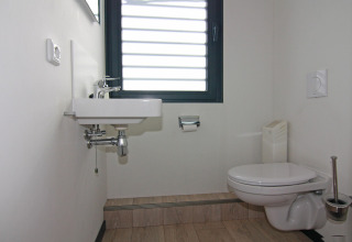 Moderne badeværelse på husbåd med væghængt toilet, håndvask, vindue og stilrent design i Tyskland.