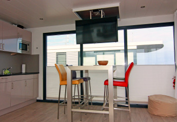 Modernes Wohnzimmer und Küche auf einem Hausboot mit Esstisch, bunten Stühlen und Deckenfernseher.
