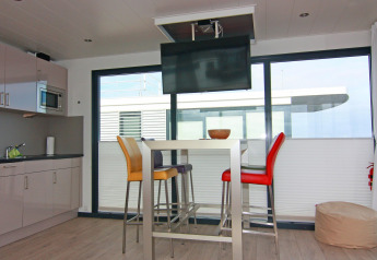 Sala de estar moderna y cocina en una casa flotante con mesa alta, sillas coloridas y televisor de techo.