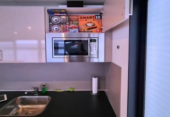 Cocina moderna en una casa flotante con fregadero, microondas, armario abierto y utensilios de limpieza en Alemania.