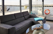 Living area on houseboat 'Leni' featuring a gray sofa, glass table, and waterfront view in Germany.