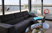 Living area on houseboat 'Leni' featuring a gray sofa, glass table, and waterfront view in Germany.