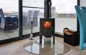 Modern wood stove on a glass plate inside a cozy houseboat living room, overlooking deck and water.