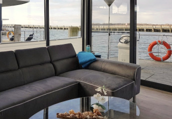 Modernes Wohnzimmer auf einem Hausboot mit schwarzem Sofa und Ausblick aufs Wasser, Ribnitz-Damgarten.