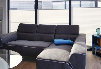 Moderne Wohnzimmer auf Hausboot mit dunkelgrauem Sofa, blauer Kissenrolle und großen Fenstern.