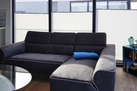 Moderne Wohnzimmer auf Hausboot mit dunkelgrauem Sofa, blauer Kissenrolle und großen Fenstern.