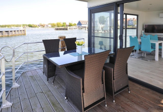 Terraza exterior del houseboat 'Leni' con mesa, sillas y vista al agua en Alemania.