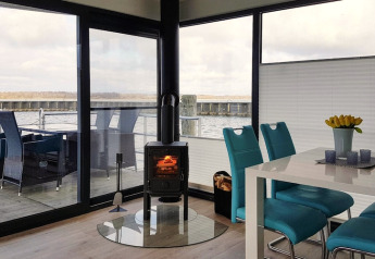 Modern houseboat interior with panoramic windows, stove, turquoise chairs, dining table and lake view.