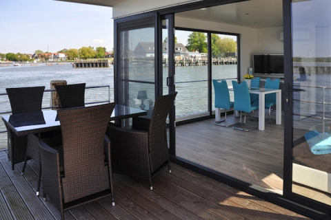 Áreas de comedor interior y exterior elegantes en una casa flotante con vistas al agua en Alemania.