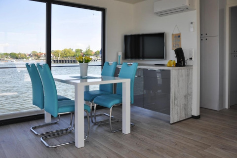 Zona de comedor moderna con sillas turquesas y vista al agua en la casa flotante 'Leni' en Ribnitz-Damgarten, Alemania.