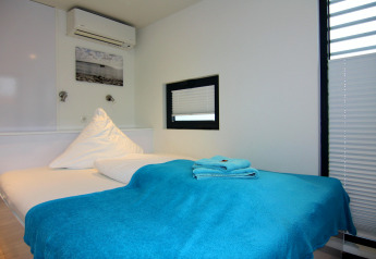 Gemütliches Schlafzimmer auf einem Hausboot mit blauer Decke, Handtüchern und modernen weißen Wänden.