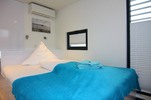 Gemütliches Schlafzimmer auf einem Hausboot mit blauer Decke, Handtüchern und modernen weißen Wänden.