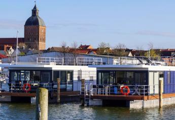 Woonboot «Floating House Luisa» te Ribnitz-Damgarten, Duitsland, met kerktoren en stad op de achtergrond.