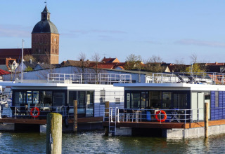 Husbåd «Floating House Luisa» på vandet i Ribnitz-Damgarten, med kirketårn og by i baggrunden.