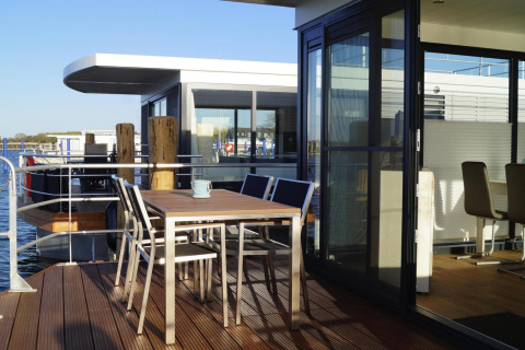 Terraza exterior del houseboat 'Floating House Luisa' con muebles modernos, luz solar y vistas al agua.