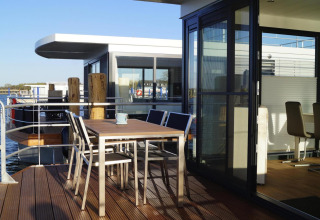Terraza exterior del houseboat 'Floating House Luisa' con muebles modernos, luz solar y vistas al agua.