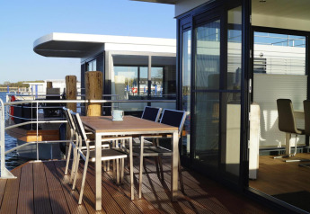 Buitenterras van woonboot 'Floating House Luisa' met moderne meubels, zonlicht en uitzicht op het water.